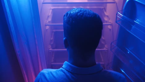 hombre abre el refrigerador vacío por la noche en la iluminación de neón. pobreza y crisis
