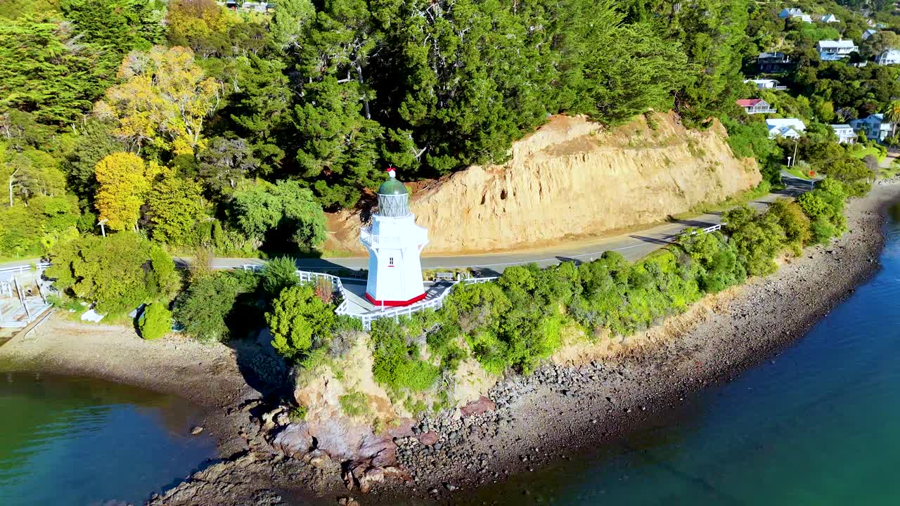 Aerial footage of Akaroa Lighthouse surrounded by lush greenery and turquoise waters under clear skies