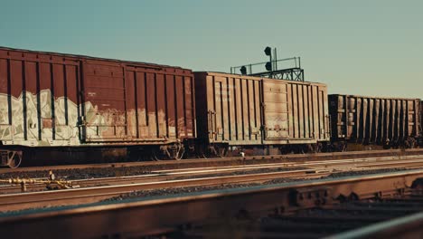 freight train cargo cars departing station at empty industrial city railway yard. locomotive wagons speed up on station rail tracks infrastructure at sunset during golden hour dusk cinematic prores 4k