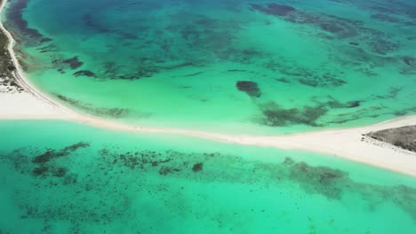 Aerial-tilt-down-view-of-Cayo-de-Agua-in-Los-Roques,-Venezuela-with-clear-turquoise-waters-and-sandy-beach