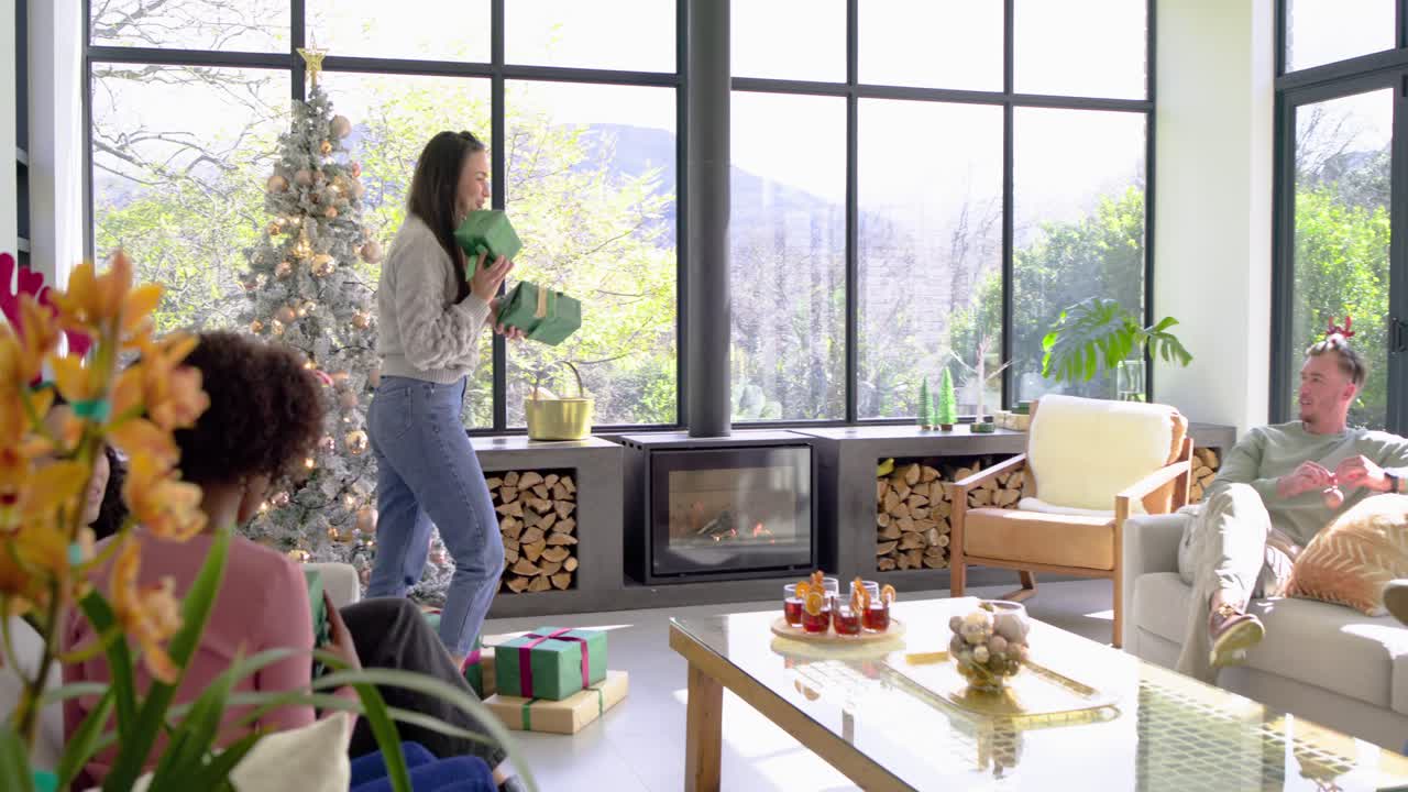 Mid adult woman in living room gathering gifts from tree, handing presents to friends for Xmas