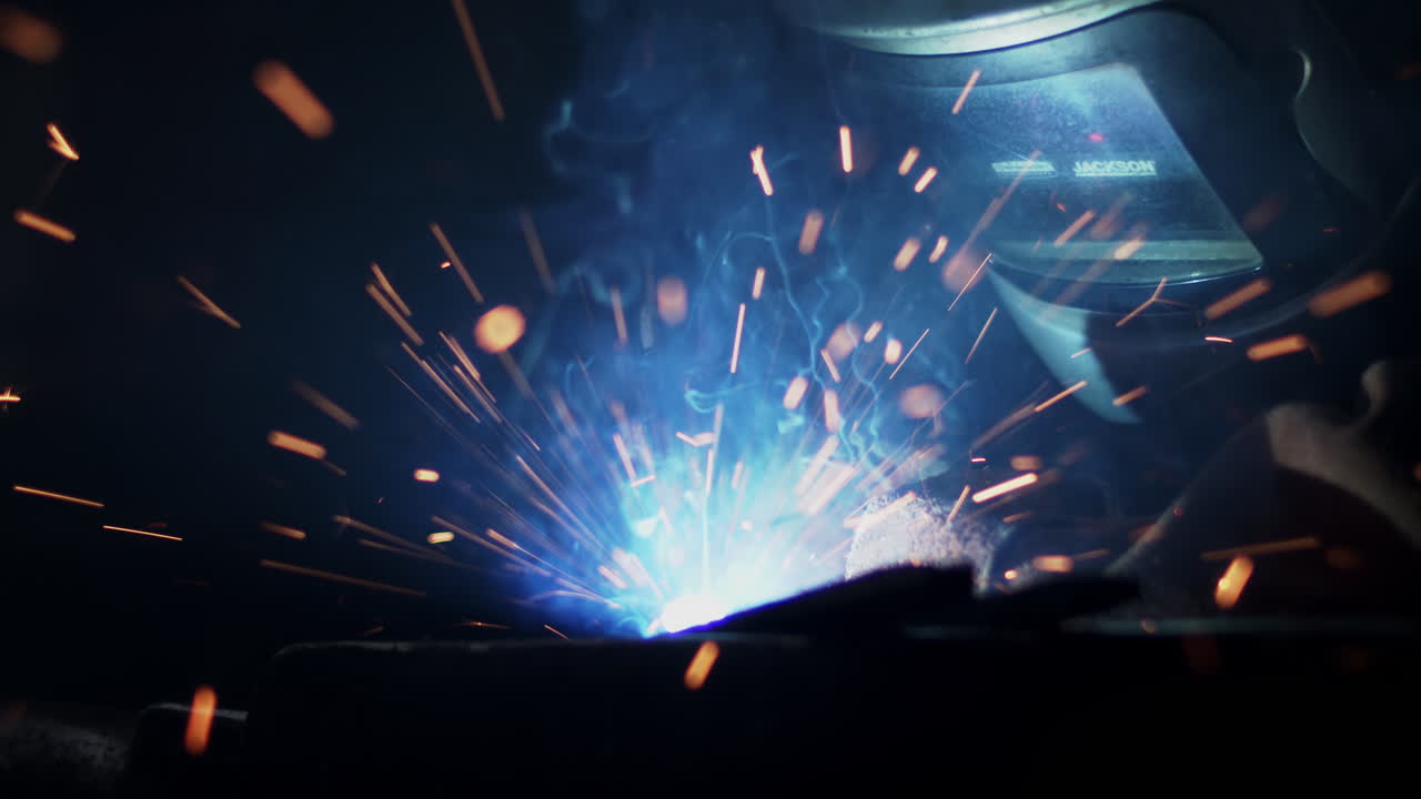 Sparks fly and smoke rises in slow motion as a welder fuses metal in a workshop