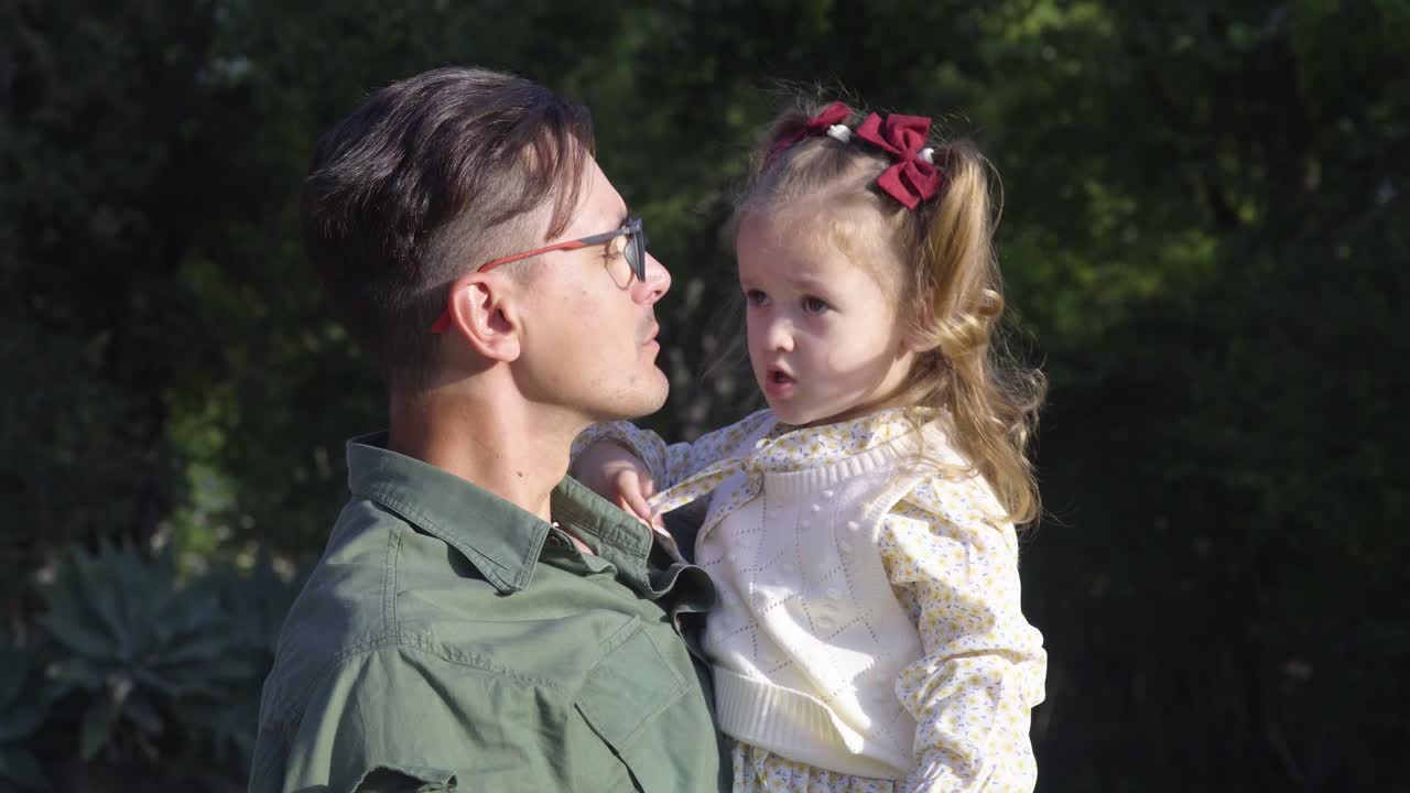 즐거운 젊은 아버지가 도시 공원에서 재미있는 딸을 키스하고 있습니다.