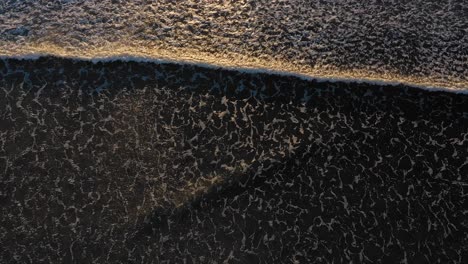 Aerial-TOP-DOWN-as-a-couple-of-wind-whipped-waves-pass-from-top-to-bottom-over-a-dark-ocean-with-cool-patterns-and-sunlight-reflecting-in-the-surf-in-York-Beach-Maine