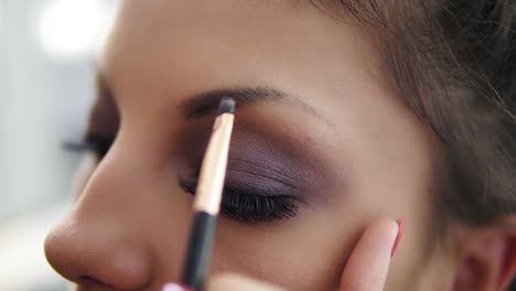 closeup view of the makeup artist's hands correcting eyebrows using special brush