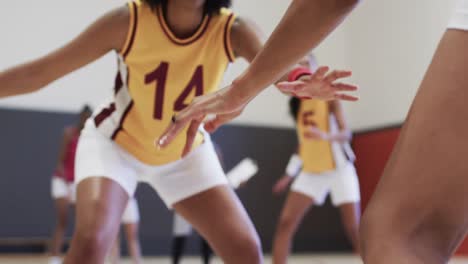 Diverse-female-basketball-team-training-with-male-coach-in-indoor-court,-in-slow-motion