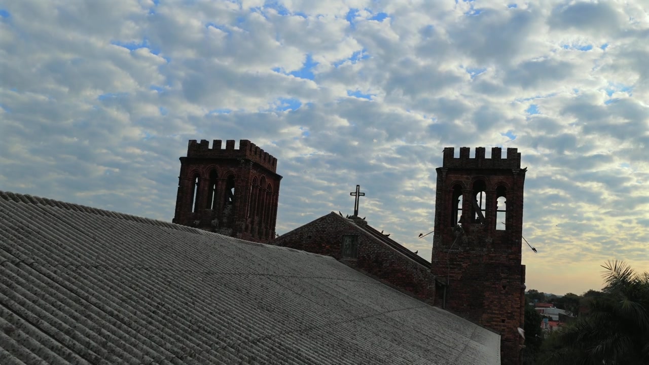 Ripresa aerea con drone del tetto di una chiesa con due torri in mattoni, croce e cielo nuvoloso a Villarrica.