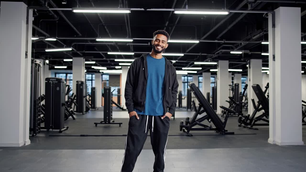 atleta masculino confiado de pie con energía positiva en un amplio y moderno gimnasio, irradiando determinación y bienestar en medio de un ambiente de fitness brillante y limpio