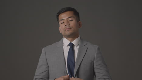 studio portrait of serious businessman straightening suit jacket and tie against grey background looking at camera