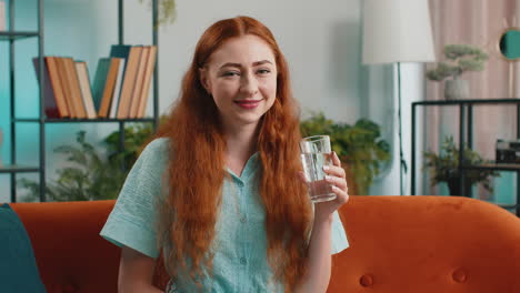 Thirsty-young-woman-sitting-at-home-holding-glass-of-natural-aqua-make-sips-drinking-still-water