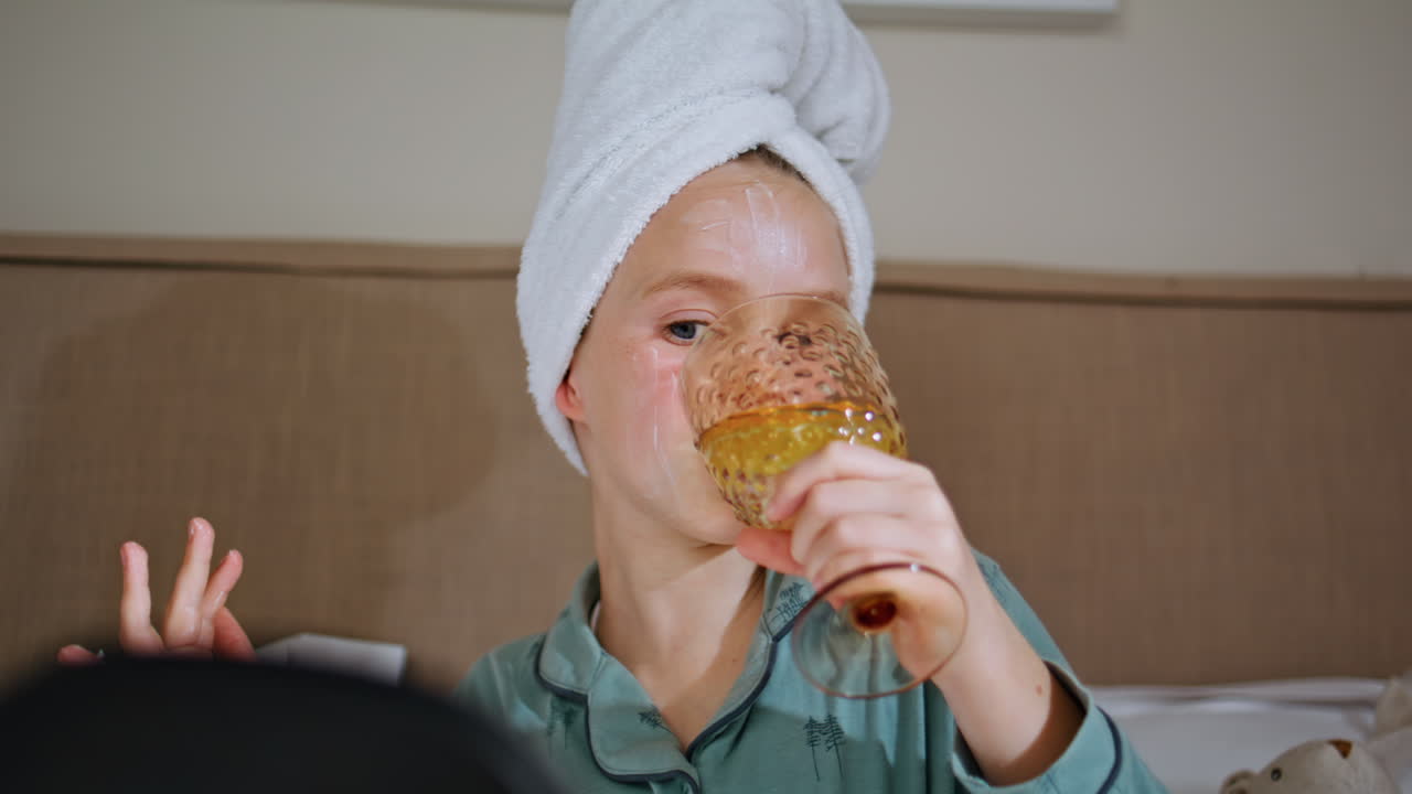 Kid rubbing face mask sipping lemonade closeup. Funny girl home spa treatment