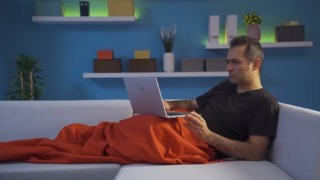 man using laptop while lying down closes laptop nervously.