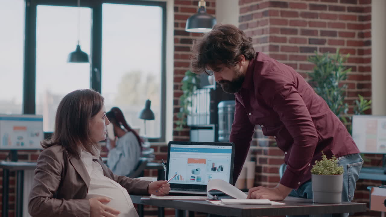 Business woman expecting child and having discussion with man while working