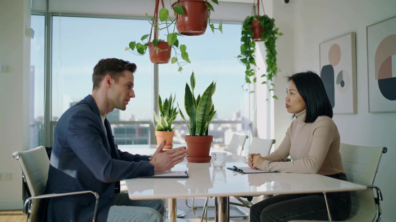 Opening exchange man in blazer gesturing while explaining points at table with plants and notepad