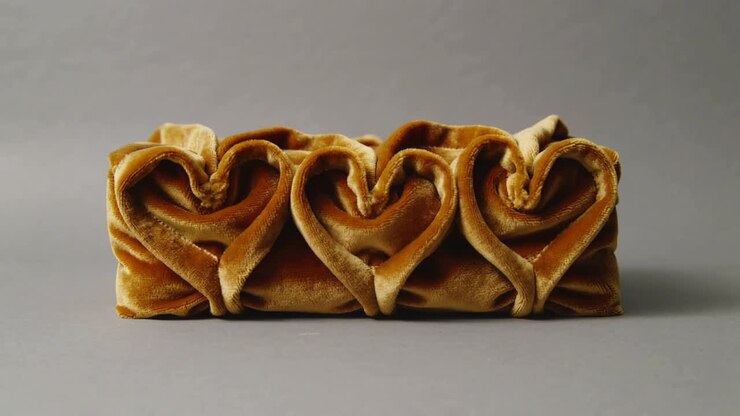 Pulling camera in around three folded golden brown velvet hearts on gray table, boosting texture
