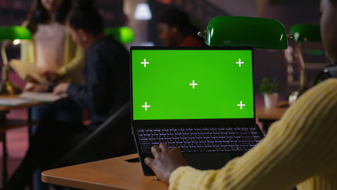 Person working on a laptop with green screen in a cafe/co-working space