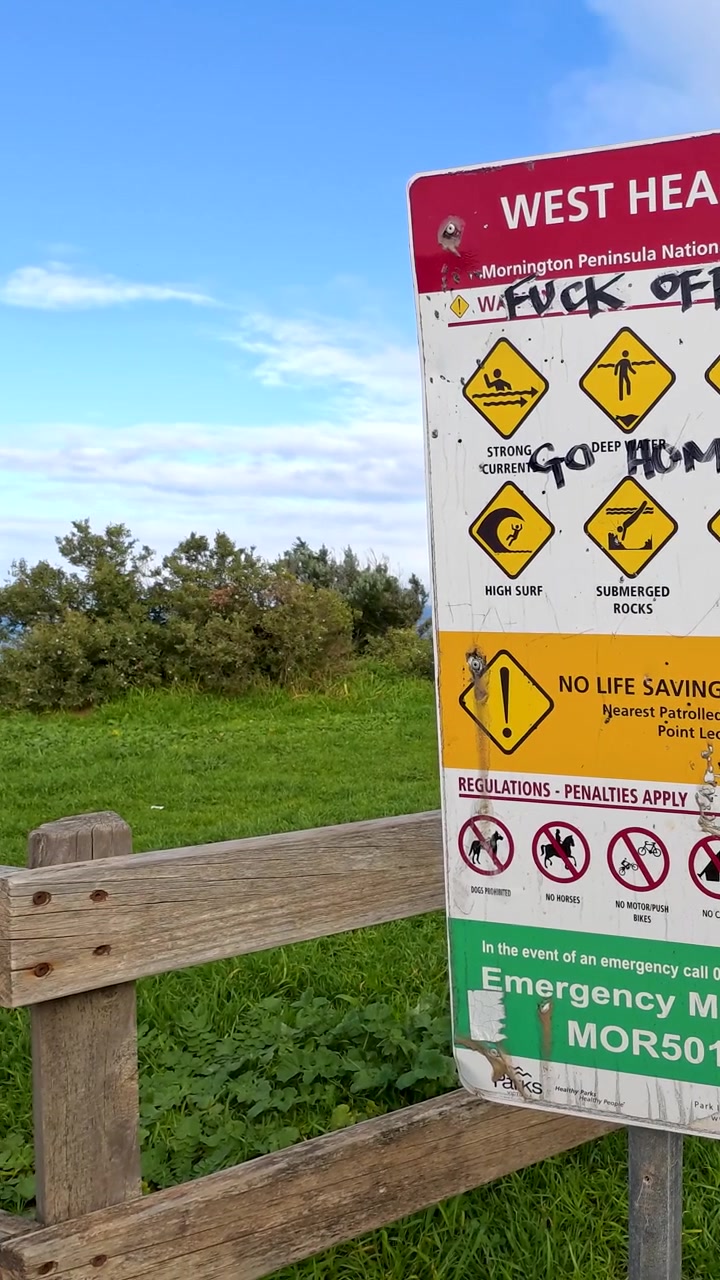 Kameran rör sig förbi en skadad säkerhetsskylt och avslöjar en naturskön grön kustudde och havet