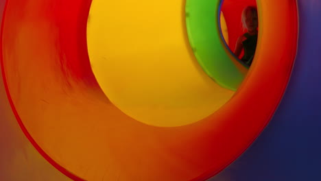 child sliding down colorful playground tube