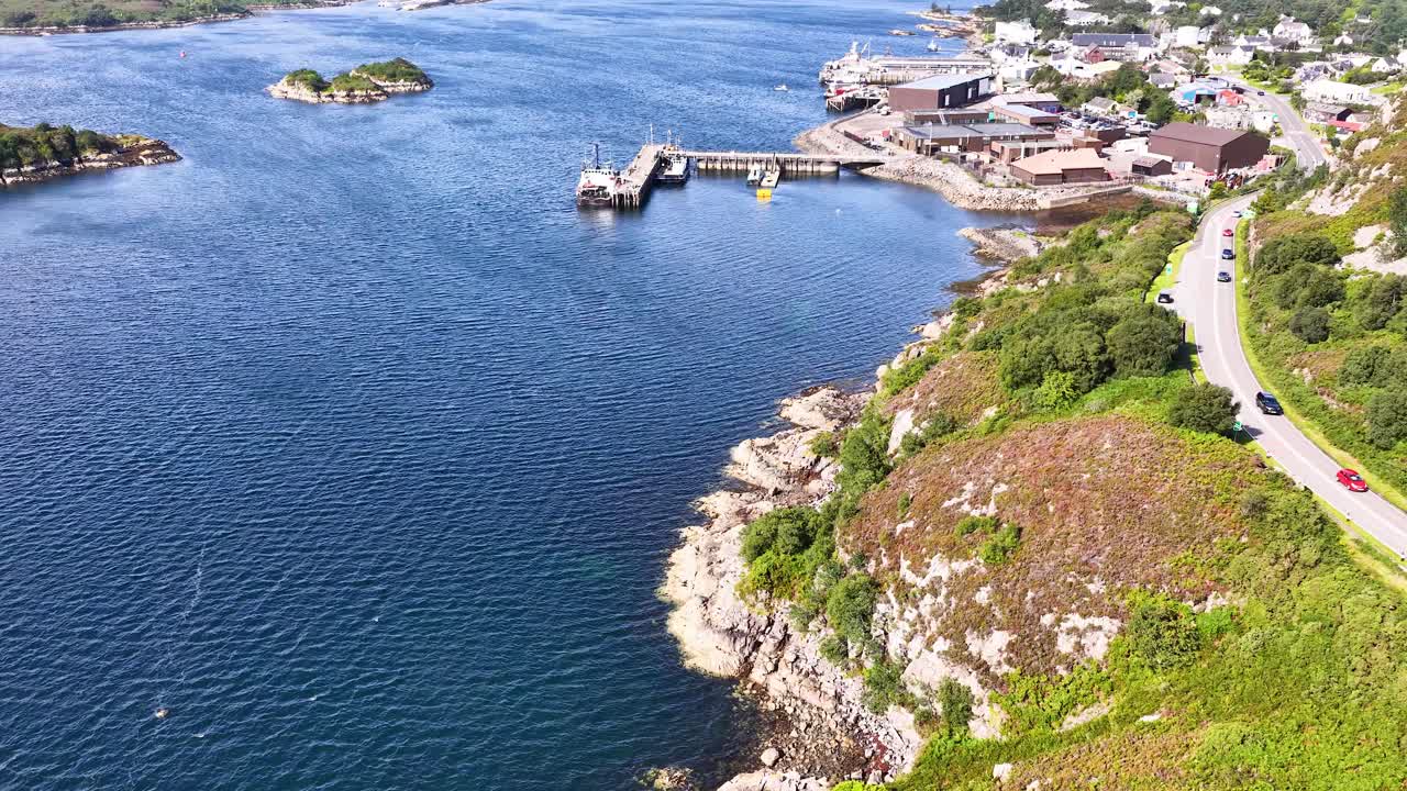 Drone glides above Dundee coastline, revealing harbor, boats, winding road, and lush summer landscape