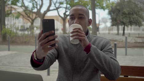 happy man drinking coffee to go and having video chat outdoor