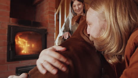 Mann-Sitzt-Mit-Frau-Zu-Hause-Am-Kamin-Und-Streichelt-Hund