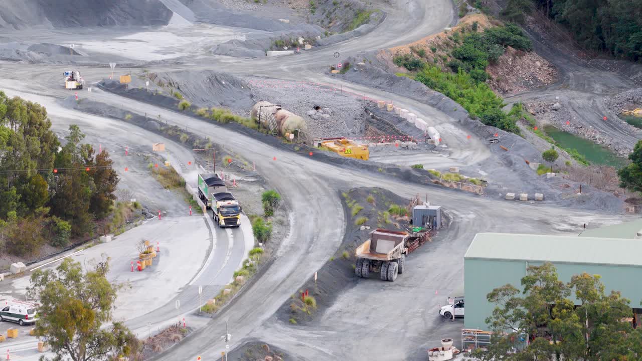 Drone footage captures vehicles and equipment in a Gold Coast quarry. Overcast lighting highlights the industrial landscape