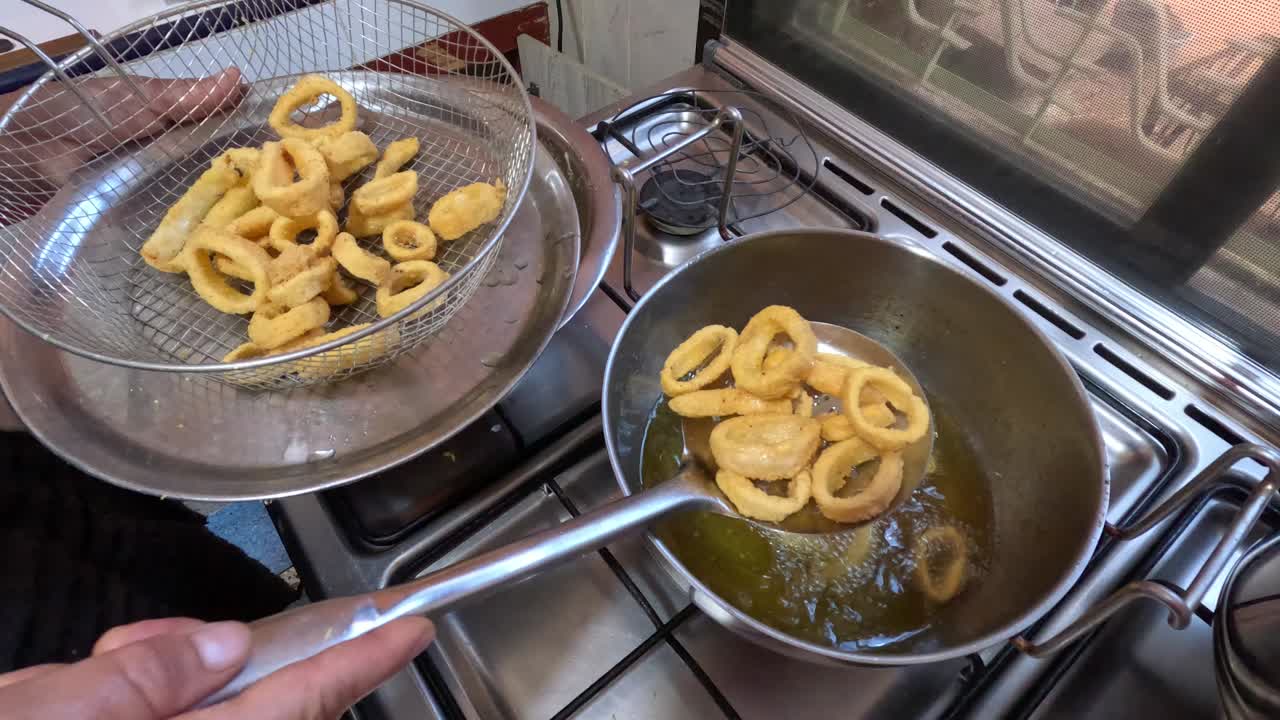 Anelli di calamari fritti croccanti alla marocchina che sfrigolano nell'olio caldo, ricoperti di pastella speziata, sollevati con una schiumarola, che mostrano un antipasto di mare dorato e croccante in un ambiente di cucina tradizionale