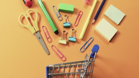 overhead view of shopping trolley and school items on orange background