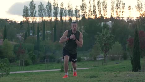 A-muscular-sportsman-doing-lunges-in-a-park,-with-the-sunset-in-the-background