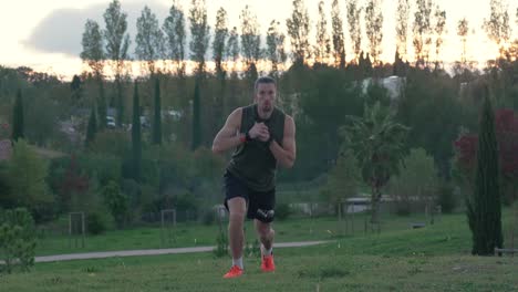 un deportista musculoso haciendo estocadas en un parque, con la puesta de sol al fondo