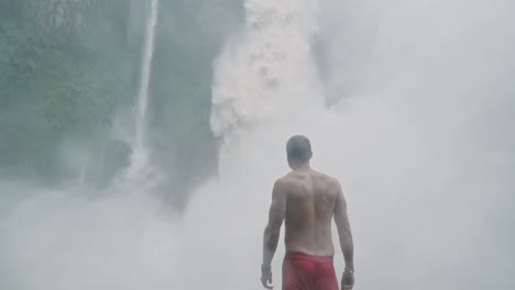 man looks up at roaring bajos del toro waterfall in costa rica, slow motion