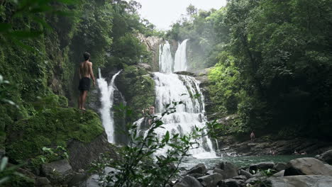 wide shot of man in front of nauyaca waterfalls costa rica jungle, slow motion