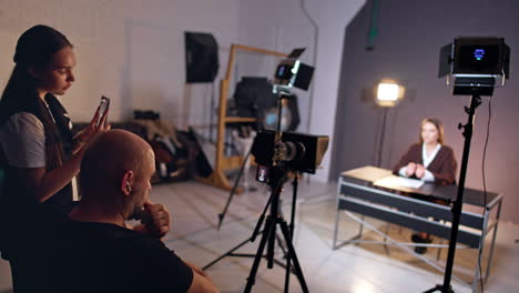 backstage of program footage in modern studio. filming crew takes video of a lady sitting at desk talking to camera