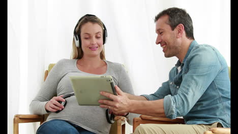 man using tablet while pregnant woman listening music on headphones