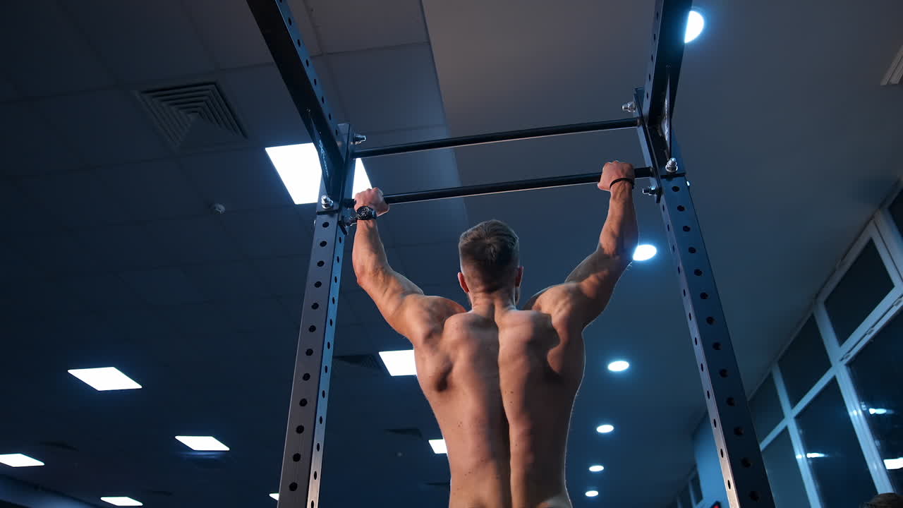 Handsome man gumped on horisontal bar. Male sportsman trains in gym. Slow motion.