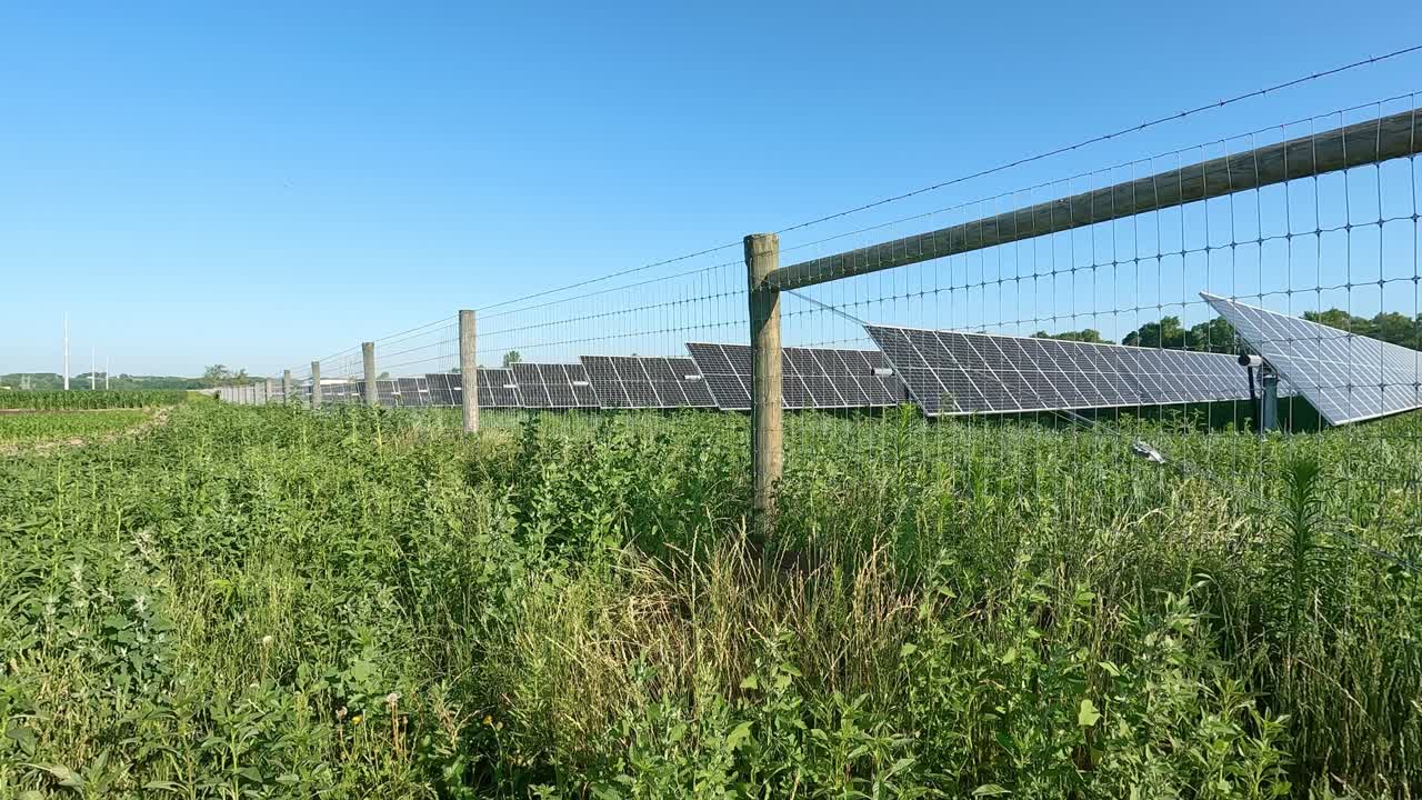 vista de una matriz de paneles solares rodeada por una valla en una zona rural con campos llenos de cultivos