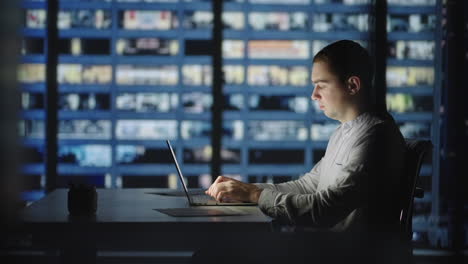 a man works on a laptop against the background of the night city