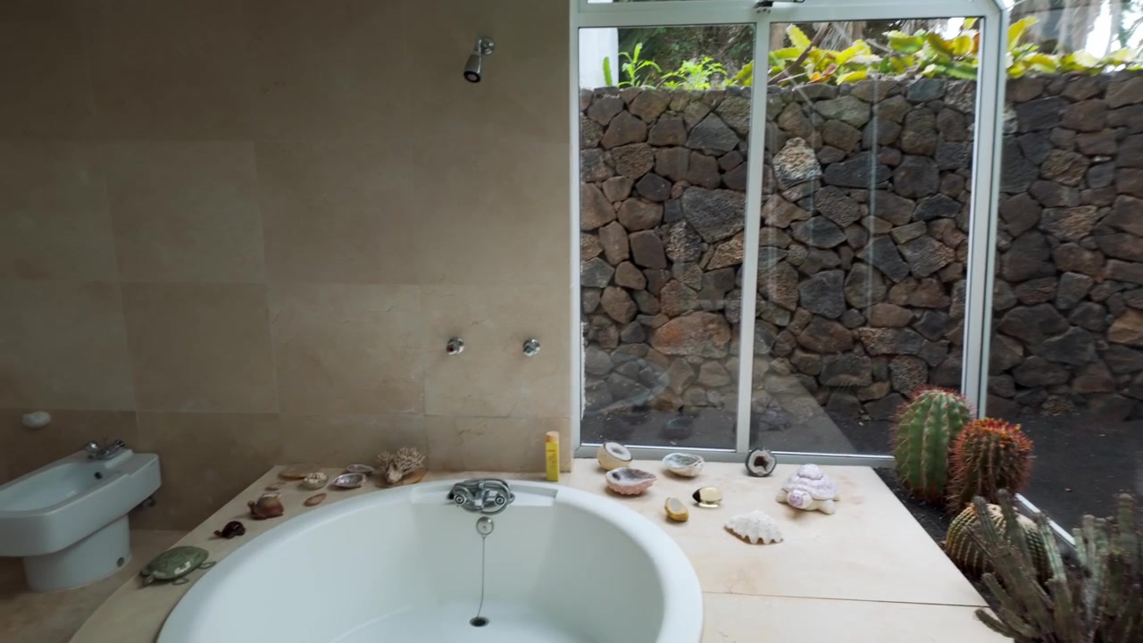 Vista de bañera redonda decorada con una gran ventana frente a una pared de roca volcánica en Haría, Lanzarote, España.