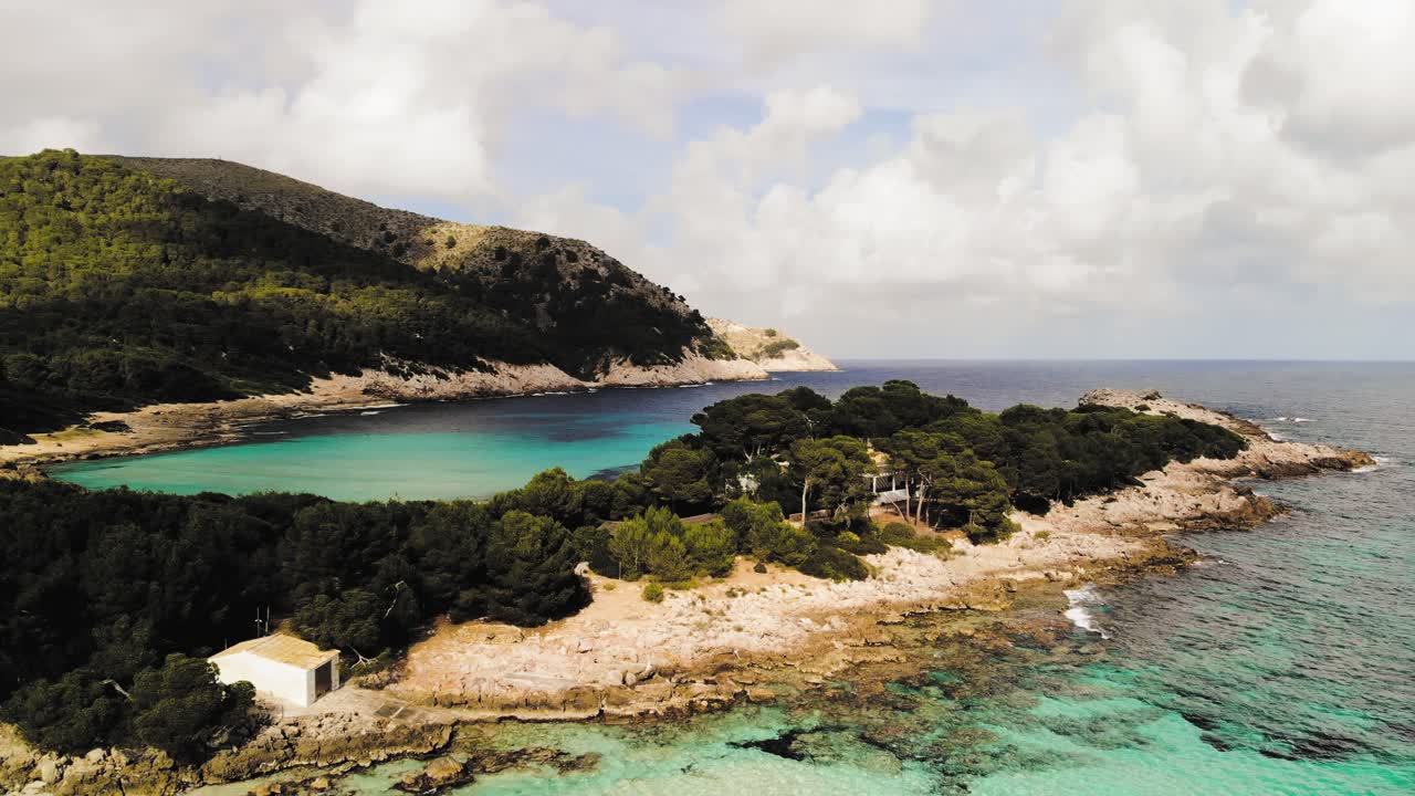 aerial drone shot of a distant isolated house surrounded by white sand beaches and clear blue water of the Mediterranean in Majorca