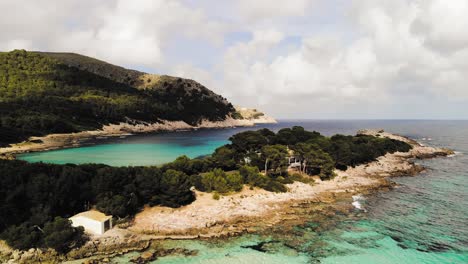 aerial drone shot of a distant isolated house surrounded by white sand beaches and clear blue water of the mediterranean in majorca