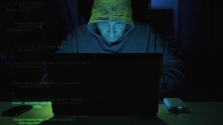 Hacker maschio concentrato che digita un codice di sicurezza su un computer portatile visibile sullo schermo sinistro. - primo piano