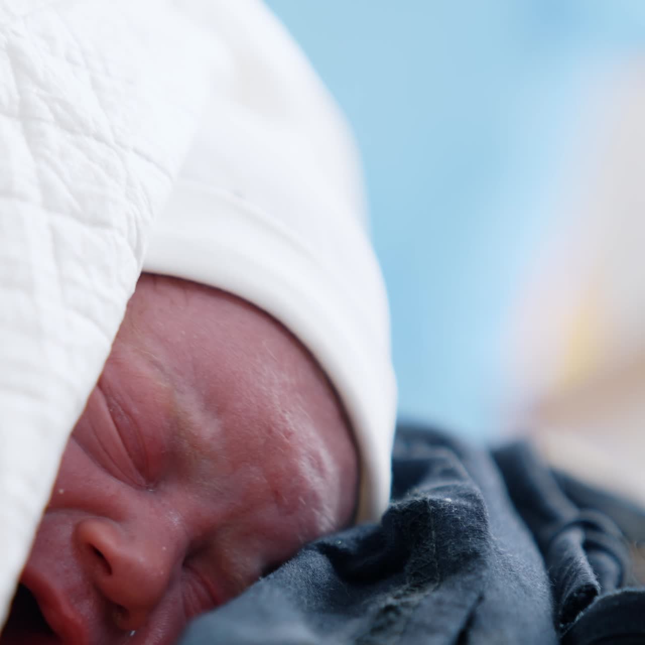 Little red crying newborn lying on his mom's chest. Just born baby covered in blankets. Close up portrait