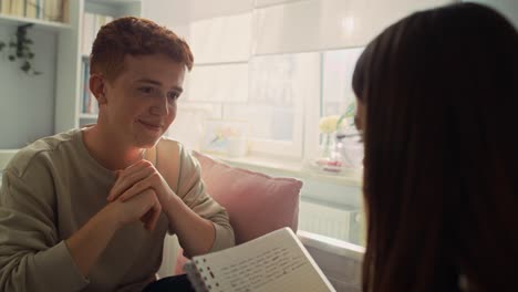 Two-caucasian-teenagers-sitting-on-bed-and-learning-from-books-with-smile