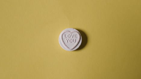 hand picking up heart candy with love you message on yellow background