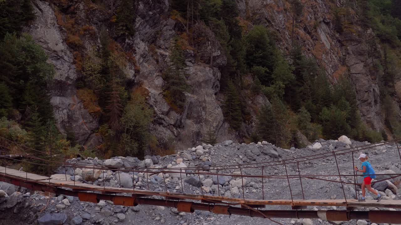 chica turista cruzando el puente viejo a través del río glacial salvaje en las montañas del cáucaso, georgia