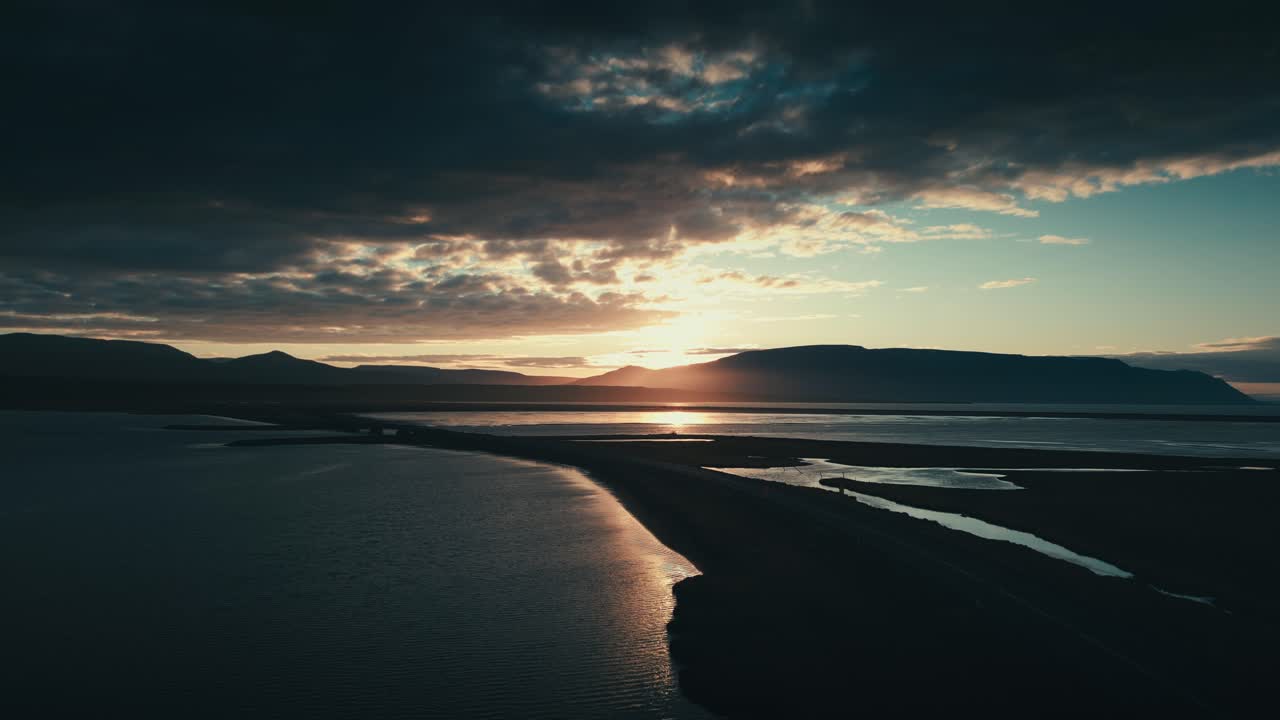increíble y épico dron y toma aérea del sol poniéndose contra un puente y una serie de lagos con montañas en la distancia