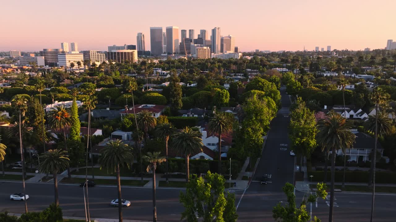 Vista aérea do cruzamento de Beverly Hills com edifícios Wilshire no horizonte, carros circulando por ruas arborizadas.