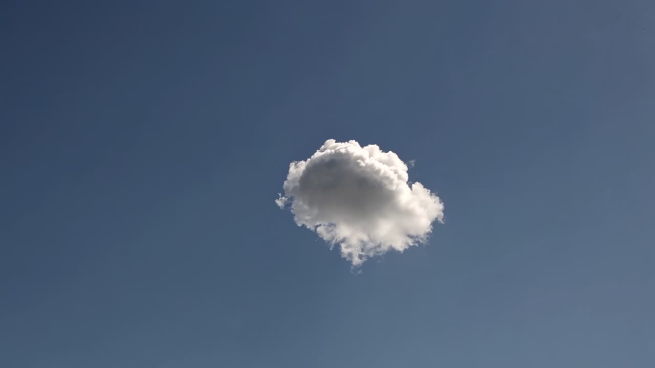 A single fluffy cloud against a clear blue sky, captured from a low-angle perspective