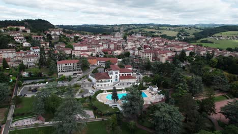 drone-shot-goinf-forward-flyng-over-Saint-Galmier-and-it's-church-to-reveal-the-landscape-behind,-loire-departement,-region-auvergne-rhone-alpes,-france