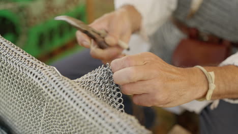 a slow pull-out shot reveals an armorer's skilled hands crafting chainmail. using pliers, he meticulously links individual metal rings to create a historic suit of armor